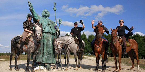 Cuatro jinetes saludando junto a estatua en el camino francés
