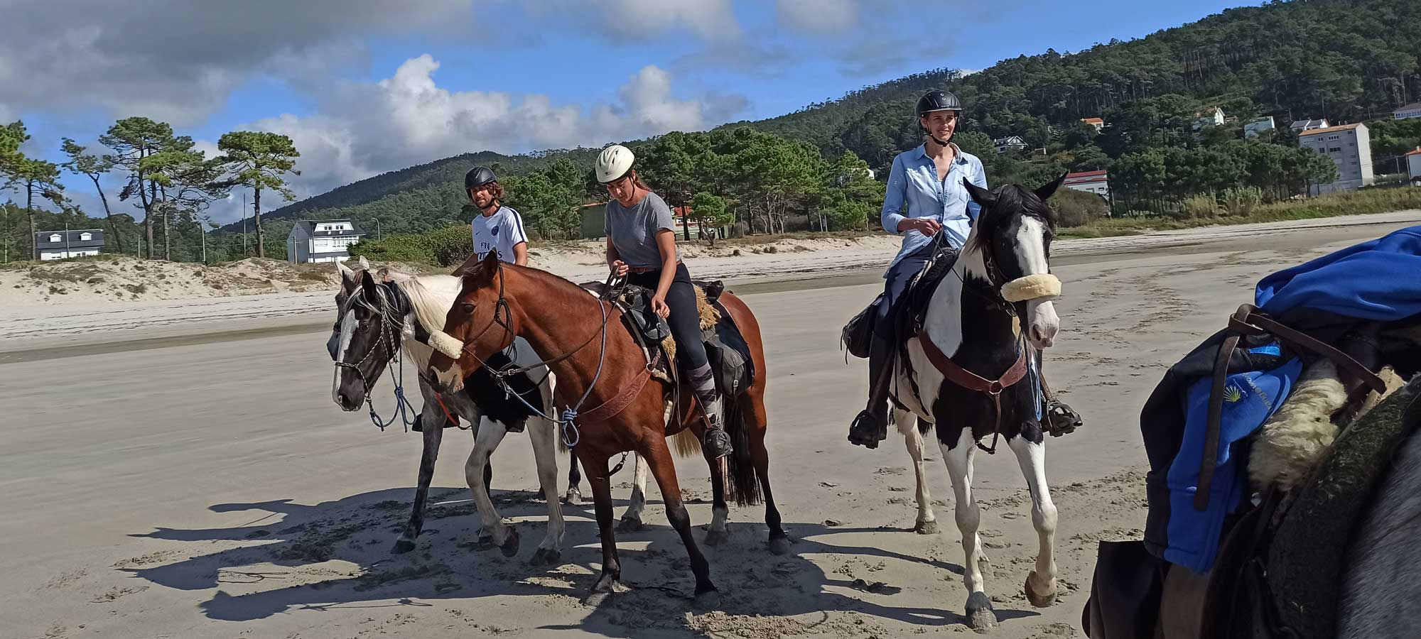 3 personas montando a caballo por la playa